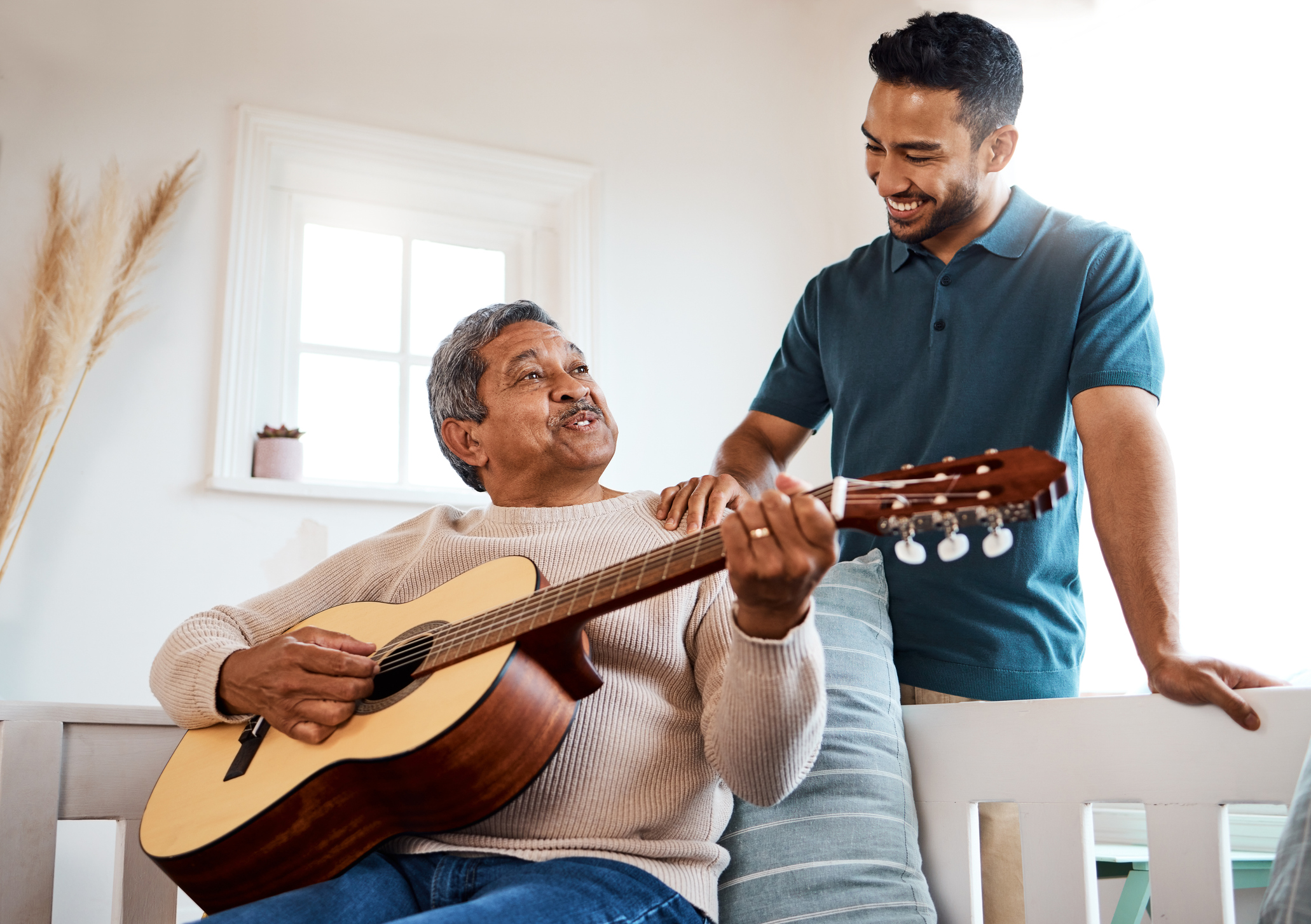 Shot of a young man listening to his father play the guitar at home